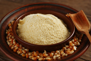 Flour and corn grains in bowls with spoon on wooden background