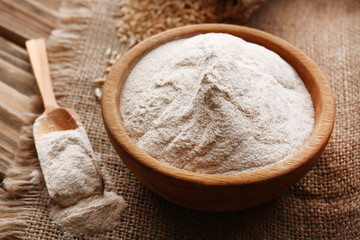 Fototapeta na wymiar Flour in bowl with grains in bag on sackcloth background