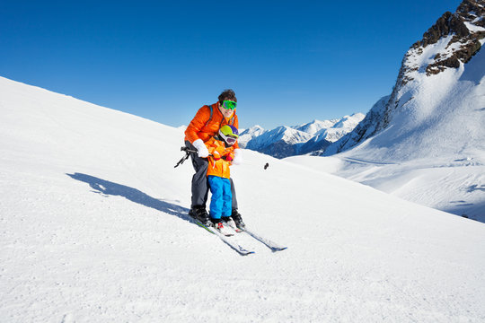 Dad teach little son to ski in mountains