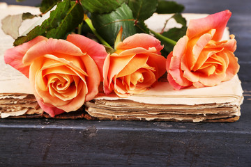 Tea roses with open old book on color wooden table, closeup