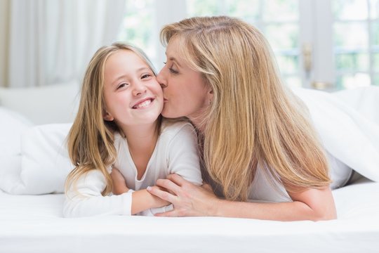 Mother kissing her daughter on the cheek in the bed