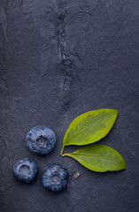 A bunch of delicious blueberries with green leaves on a dark bla