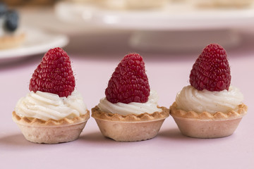 Sweet tartlets filled with cream and raspberry on pink backgroun