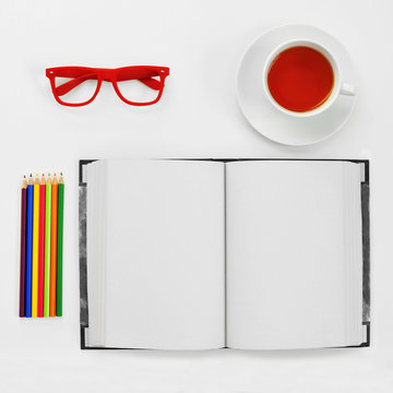 colored pencils, blank notebook, eyeglasses and cup of tea on a