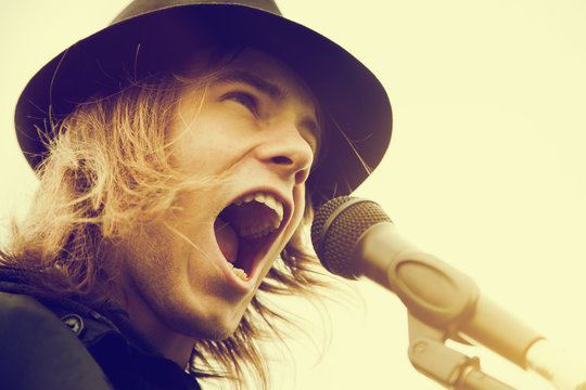 Man with long hair and hat shouting to microphone. Vintage music