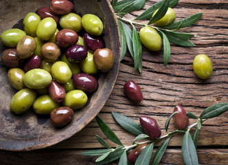 Wooden bowl full of olives and olive twigs besides it.