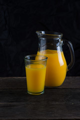 Vintage jug and glass with orange juice, on dark background