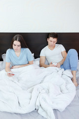 couple with smartphones in pajamas in their bed searching or bro