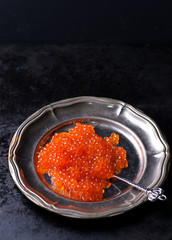 Salmon caviar on metal plate on dark background