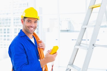 Smiling male electrician holding multimeter in office