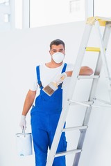 Handyman with paintbrush and can leaning on ladder at home