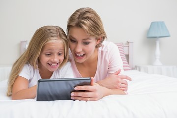 Mother and daughter using tablet together on bed