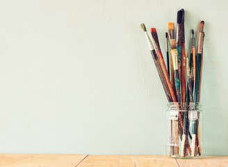 paint brushes in jar over wooden aqua blue background