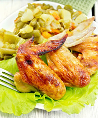 Chicken wings fried with vegetables in plate on board