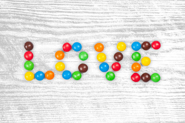 glazed color candy write word love isolated on white wood backgr