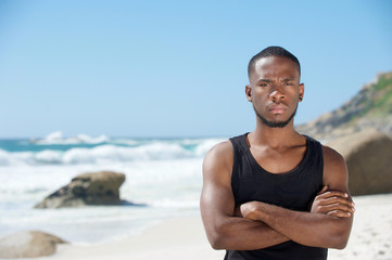 Handsome young man standing at the beach with arms crossed