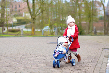 Toddler girl walking with toy stroller in the park