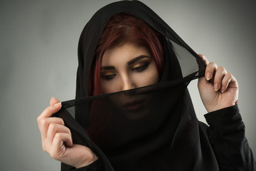 Young muslim woman covering her face and hair with a black veil