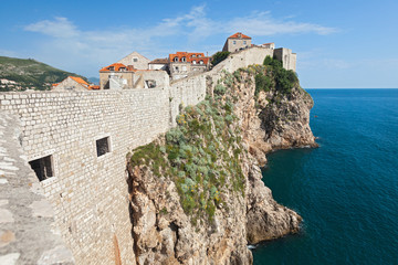 Fototapeta na wymiar DUBROVNIK, CROATIA - MAY 26, 2014: Old city walls build on cliffs and houses inside the walls. City wall is one of most popular tourist attraction in Dubrovnik.