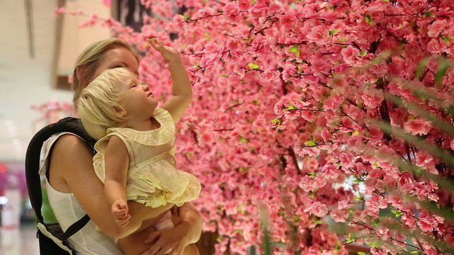 child touches sakura flowers sitting on mother arms	