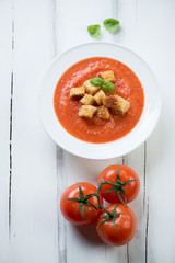 Glass plate with Gazpacho over white wooden background