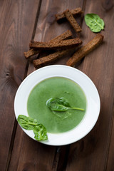Spinach cream soup with croutons over dark wooden background