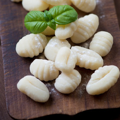 Raw gnocchi with green basil, rustic wooden surface, close-up