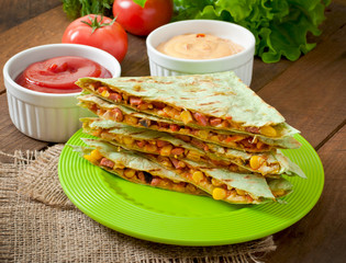 Mexican Quesadilla sliced with vegetables and sauces on the tabl