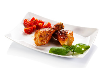 Grilled chicken legs and vegetables on white background