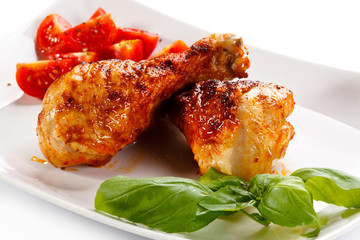 Grilled chicken legs and vegetables on white background