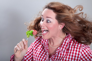 Frau in Tracht schielt und isst Rohwurst mit Salat mit fliegenden Haaren Porträt