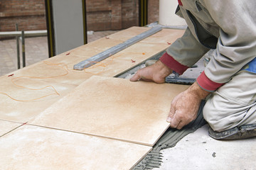 Home improvement, renovation - handyman laying tile with level - obrazy, fototapety, plakaty
