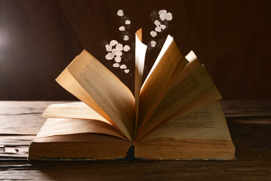 Open book with falling petals on table on dark background