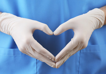 Doctor showing shape of heart by his hands in sterile gloves,