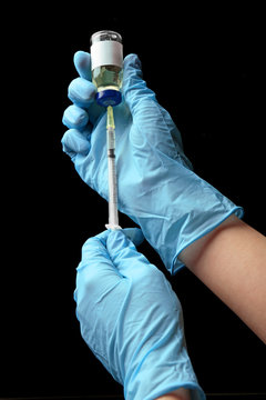 Hands in gloves filling medicine from ampule into syringe