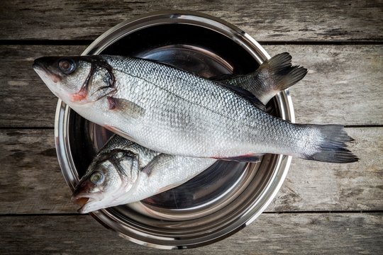 two raw fresh sea bass in a bowl on wooden table