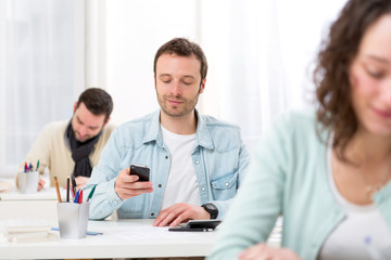 Young attractive student using his mobile during classes