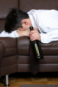 Alkoholiker liegt betrunken mit Flasche auf sofa