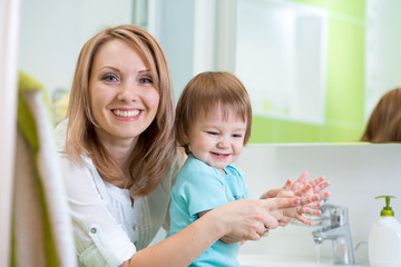 Obraz na płótnie Canvas Happy mother and child washing hands with soap in bathroom