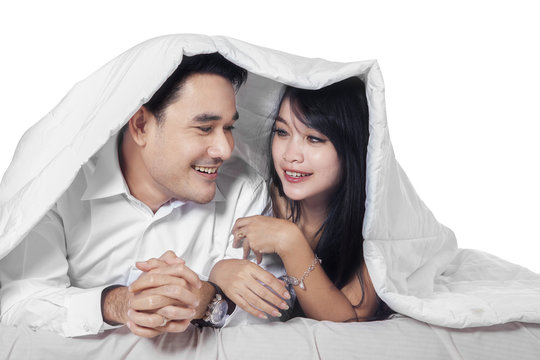 Hispanic couple on bed under blanket