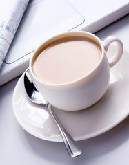 cup of coffee near the laptop and newspapers.