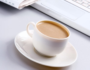 Cup of coffee near the laptop and newspapers