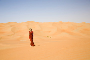 Fototapeta na wymiar Long dressed woman walks in desert