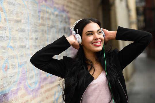 Woman in urban background listening to music with headphones