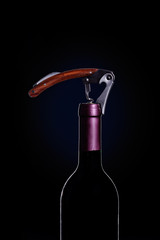 Corkscrew open wine bottle over black background