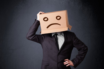 Businessman gesturing with cardboard box on his head with sad fa