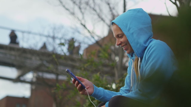 Attractive hooded woman using her phone in slow motion outdoors