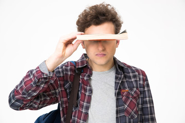 Young man covering his eyes with book over gray background