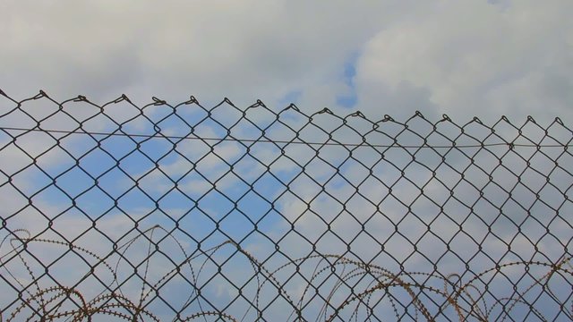 Barbed wire and metal fence on the gray clouds background.