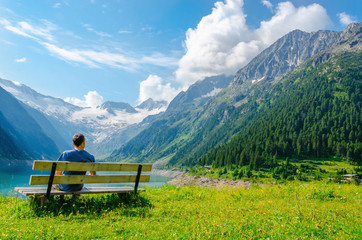 A young man sits on bench beside an azure mountain lake